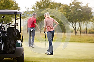 Rear View Of Couple Getting Out Of Golf Buggy To Play Shot On Green