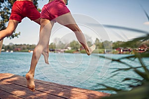 Rear view of couple holding hands jumping on wooden jetty toward water. Young man and woman having fun together. Holiday,