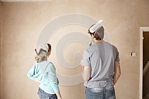 Rear View Of Couple With Paint Roller Looking At Wall
