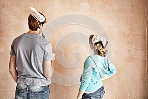 Rear view of couple with paint roller looking at wall in unrenovated room