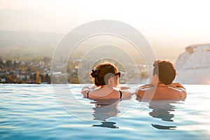 Rear view of couple relaxing at luxury resort on outdoor pool. Romantic summer vacation. People in edge swimming pool