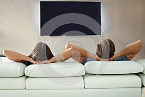 Rear view of a couple relaxing on a sofa and watching TV at home.