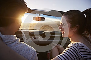 Rear View Of Couple On Road Trip Driving Classic Convertible Car Towards Sunset