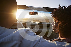 Rear View Of Couple On Road Trip Driving Classic Convertible Car Towards Sunset