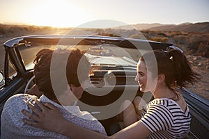 Rear View Of Couple On Road Trip Driving Classic Convertible Car Towards Sunset