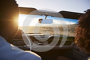 Rear View Of Couple On Road Trip Driving Classic Convertible Car Towards Sunset