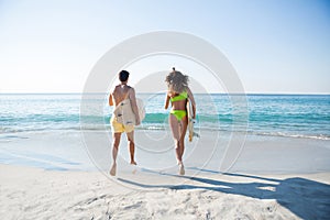 Rear view of couple running together while holding surfboards at beach