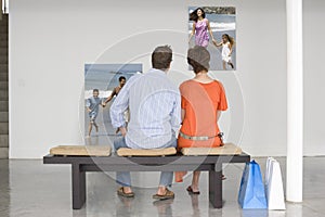 Rear view of couple seated on bench looking at photographs representing future planning