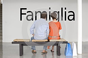 Rear view of couple seated on bench reading Italian text Famiglia (family) on wall photo