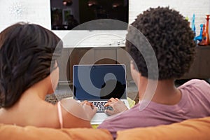 Rear View Of Couple Sitting On Sofa Using Laptop