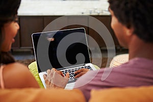 Rear View Of Couple Sitting On Sofa Using Laptop