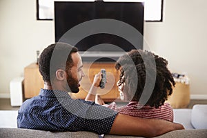 Rear View Of Couple Sitting On Sofa Watching TV Together