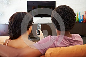 Rear View Of Couple Sitting On Sofa Watching TV Together