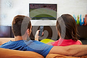 Rear View Of Couple Sitting On Sofa Watching TV Together