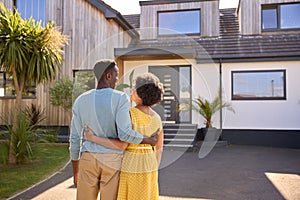 Rear View Of Couple Standing In Driveway In Front Of Dream Home Together