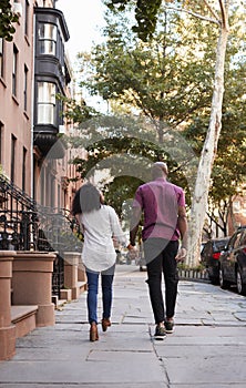 Rear View Of Couple Walking Along Urban Street In New York City