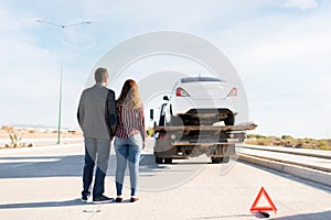 Rear view of a couple watching their car on a tow truck