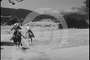 Rear view of cowboys on horses galloping through prairie land