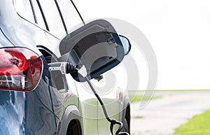 Rear view of dark blue electric car showing close up of charge cable plugged in charging the car