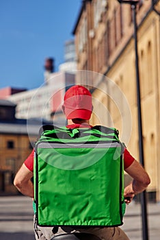 Rear view of delivery man with thermo bag riding bicycle along the street on a sunny day