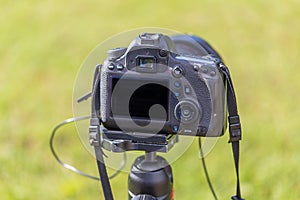 Rear view of a digital camera. The display and rear controls are visible. The camera is mounted on a tripod. The background is