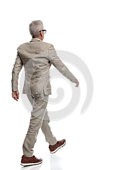 rear view of elegant old man in suit walking on white background