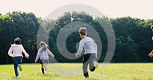 Rear view of elementary school kids running on the grass