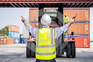 Rear view of engineer in reflective clothing with safety helmet is working and checking at containers cargo on shipping port area