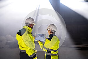 Rear view of engineers standing on construction site, holding tablet.