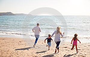 Rear View Of Family On Beach Running Across Sand Towards Sea photo