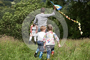 Rear View Of Family Flying Kite In Countryside