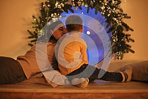 Rear view of family mother with little son looking out window on Christmas Eve at home, selective focus. Mom and kid sitting on