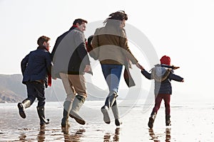 Rear View Of Family Running Along Winter Beach