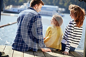 Rear view of family sit on pier in autumn day. Fall family portrait