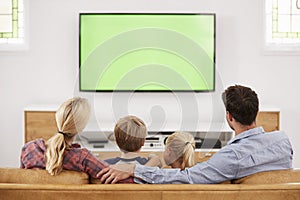 Rear View Of Family Sitting On Sofa In Lounge Watching Television