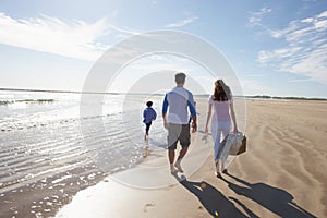 Rear View Of Family Walking Along Beach With Picnic Basket