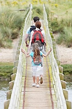 Rear View Of Family Walking Along Wooden Bridge