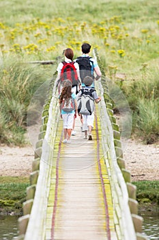Rear View Of Family Walking Along Wooden Bridge