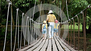 Rear view of family walking on suspension wooden bridge with rope handrails in the park.