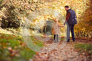 Rear View Of Father And Daughter Holding Hands On Family Walk Along Track In Autumn Countryside