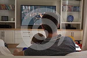 Rear view of father and son sitting at home together watching sport event on tv