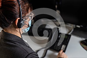 Rear view of female call center operator in mask at work table. Woman working at the reception during a pandemic