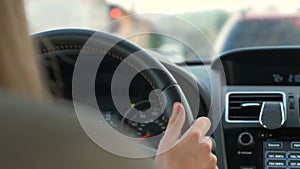 Rear view of female driver behind steering wheel driving a car on a city street.