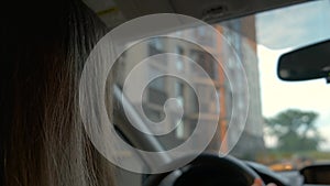 Rear view of female driver behind steering wheel driving a car on a city street.