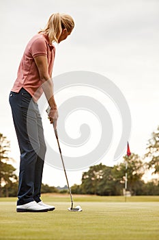 Rear View Of Female Golfer Putting Ball On Green