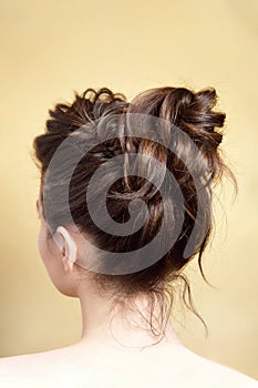 Rear view of female hairstyle medium bun on long straight brown hair with radical volume.