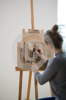 Rear view of female painter draws on the easel human figure