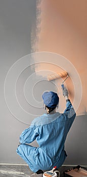 Rear view of a female painter squatting painting a wall with a paint roller