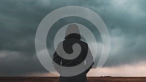 Rear view of female person wearing hooded jacket against dark moody dramatic clouds at sky