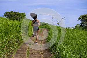 Rear view female runner training on countryside road - young attractive and fit jogger woman doing running workout outdoors at